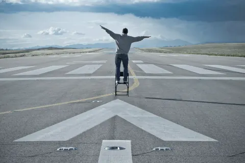 A person standing on a small ladder with arms outstretched on an open roadway.