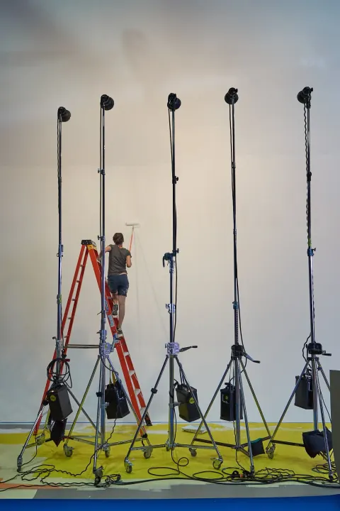 A row of tall lighting stands and ladders in a studio.