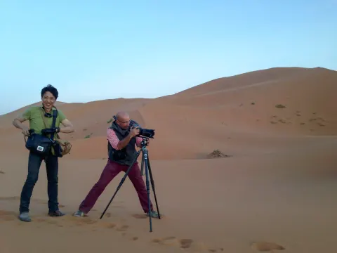 A photographer and companion working among red sand dunes.