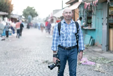 A man with a camera and backpack on a cobbled market street.