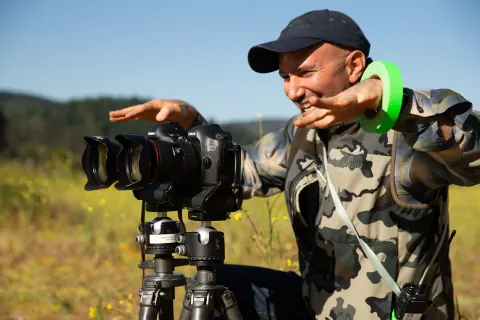 A photographer gesturing over two cameras mounted on a tripod outdoors.