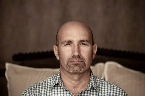 Close portrait of a bald man in a checked shirt.