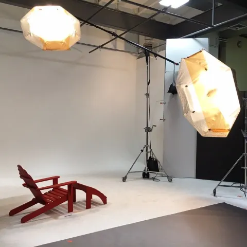 A studio set with hanging softboxes and a wooden chair on its side.