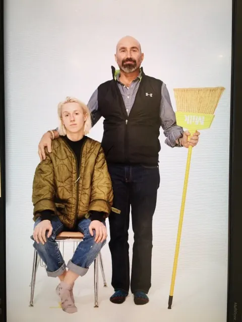 A seated woman and a standing man holding a yellow paddle against a white backdrop.
