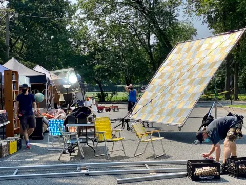 A film crew working outdoors beside a large angled reflector.