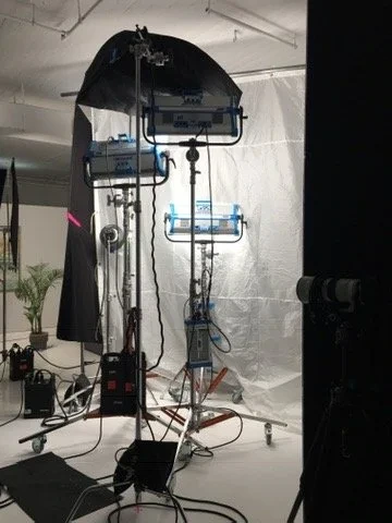 Lighting stands and overhead modifiers surrounding a chair in a studio.