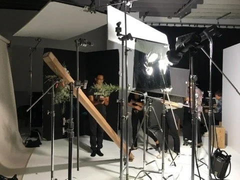 A crew member among lighting stands and angled panels in a studio.