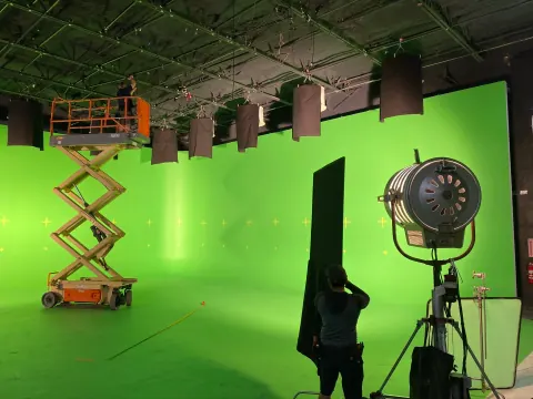 A green-screen studio with an orange lift and a large fan.