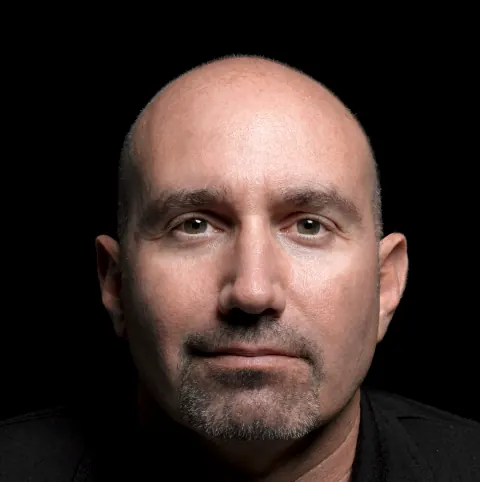 Close portrait of a bald man against a dark background.