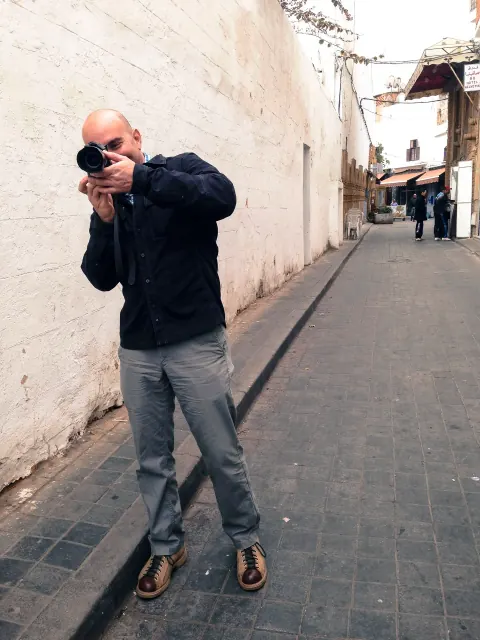 A photographer holding a camera to his eye in a narrow outdoor passage.