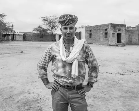 A black-and-white portrait of a man in a patterned cap standing outdoors.