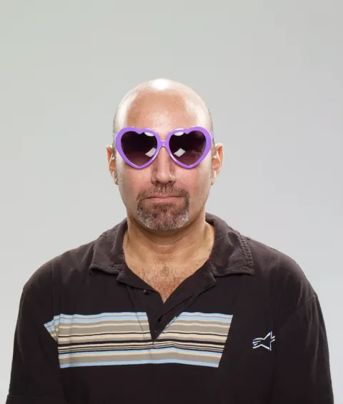 A bald man wearing purple novelty glasses and a striped polo shirt.