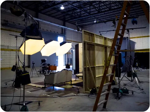A studio lighting setup with a tall ladder and wooden set walls.