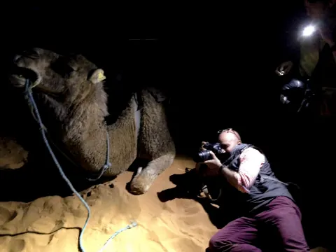 A photographer crouching beside a camel at night.