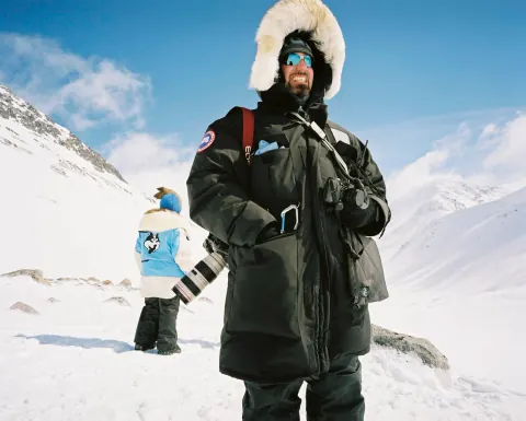 A person in heavy winter clothing standing in a snowy mountain landscape.