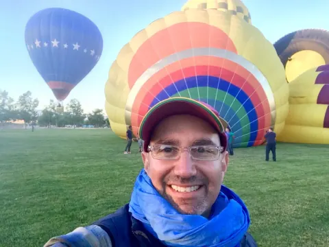 A smiling man taking a selfie in front of colourful hot-air balloons.