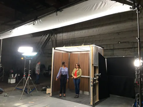 Two people posing in a small wooden set inside a studio.