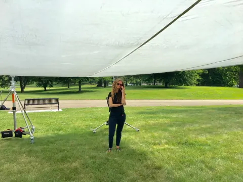 A woman standing on grass beneath a large overhead diffusion screen.