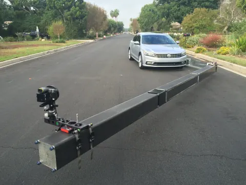 A camera mounted on a long low rig in front of a parked car.