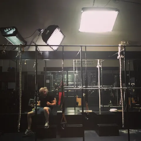 A seated person surrounded by scaffolding and overhead studio lights.