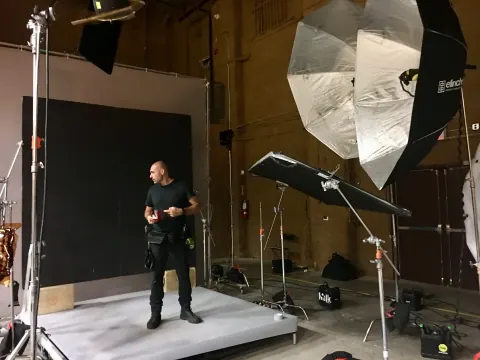 A man holding a camera on a white platform beneath studio lights.