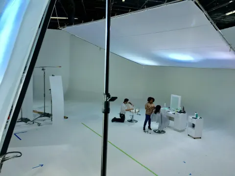 A crew sitting on a large white studio set beneath an overhead screen.