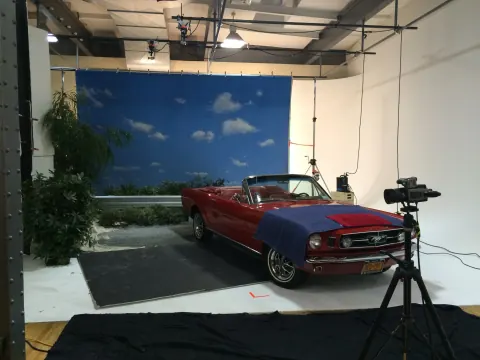 A red classic car on a studio set with a blue sky backdrop.