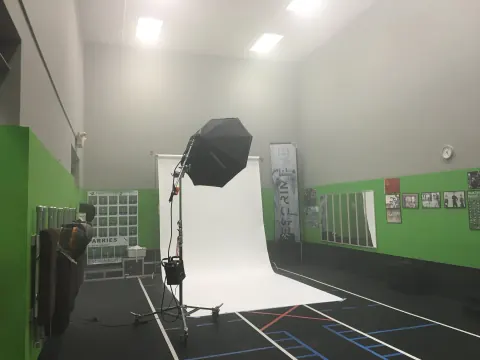 A black softbox aimed at a white paper backdrop in a green-walled room.