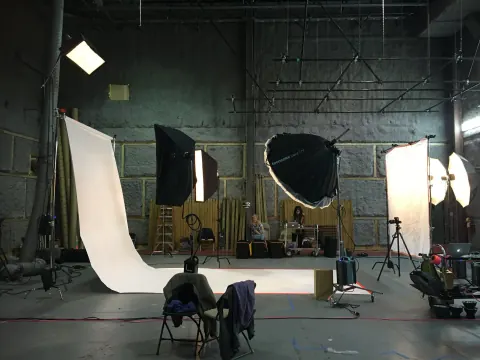 A crew and lighting equipment surrounding a white sweep in a dark studio.