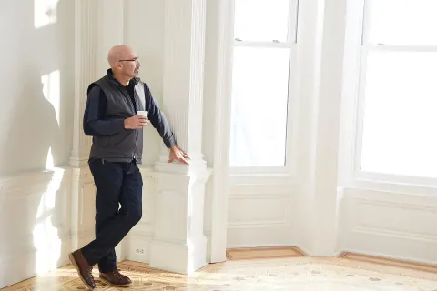 A man leaning beside a white column in a sunlit interior.