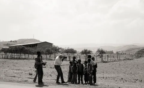 A monochrome outdoor scene with a photographer and a group of children.