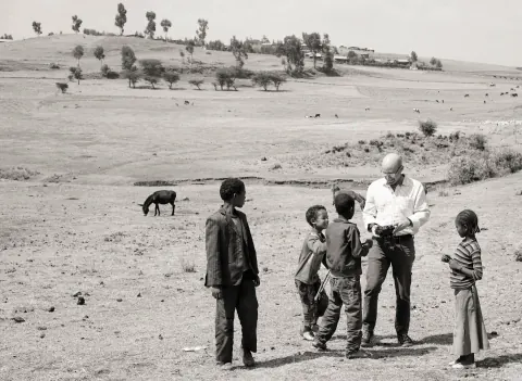 A black-and-white photograph of a man and children gathered on open ground.