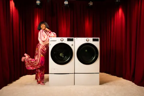 A woman in pink standing beside two washing machines in a red-curtained room.