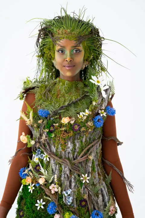 A person wearing a costume made of grass, branches and flowers.