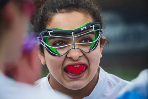 Close-up of a lacrosse player wearing green protective goggles and a red mouthguard.