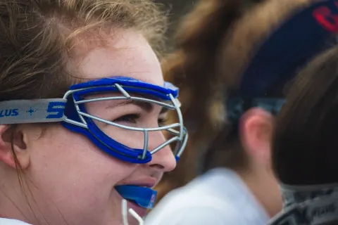 Side view of a lacrosse player wearing blue goggles and a blue mouthguard.