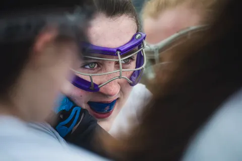 A lacrosse player in purple goggles and a blue mouthguard.