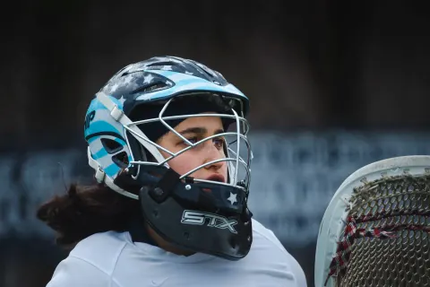 A helmeted lacrosse player looking to the side with a stick nearby.