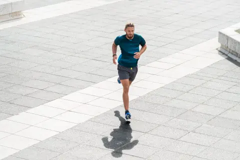 A man in a teal shirt running across a pale stone plaza.