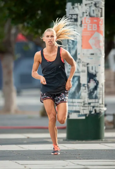 A woman running along a city street beside a poster-covered pole.