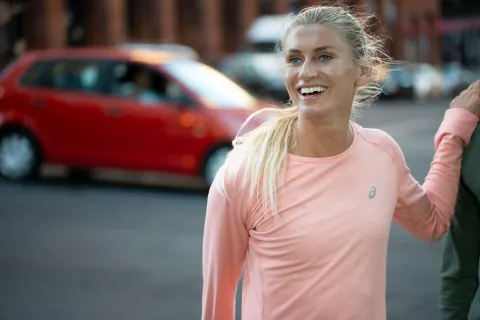 A smiling woman in a pink long-sleeved top on a city street.