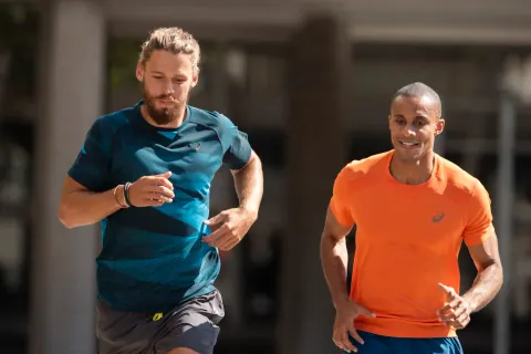Two men in teal and orange shirts running together.