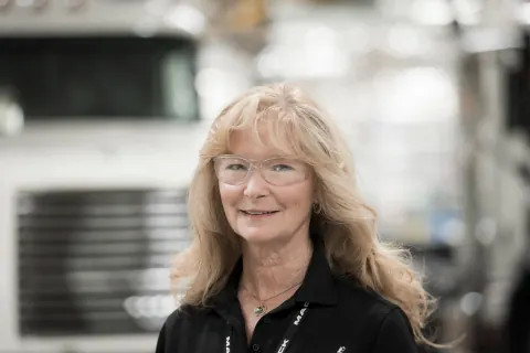 A smiling woman in a black polo shirt in a factory.
