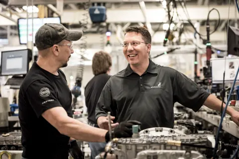 Two men talking beside machinery on a factory floor.