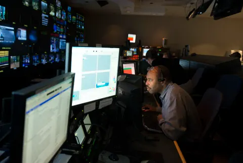 A person working at computer monitors in a dark control room.