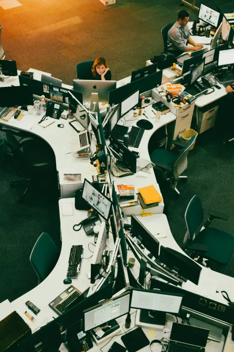 Overhead view of people working at desks in a busy circular newsroom.
