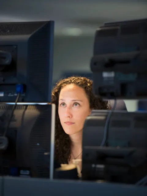 A woman looking between rows of computer monitors.