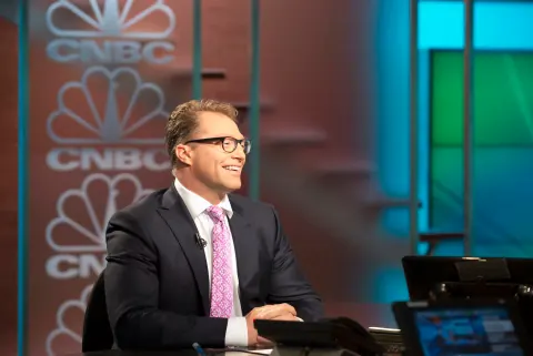 A smiling man in glasses and a suit at a CNBC studio desk.