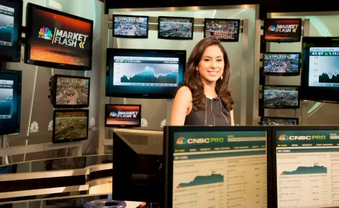 A smiling woman at a desk surrounded by Market Flash screens.