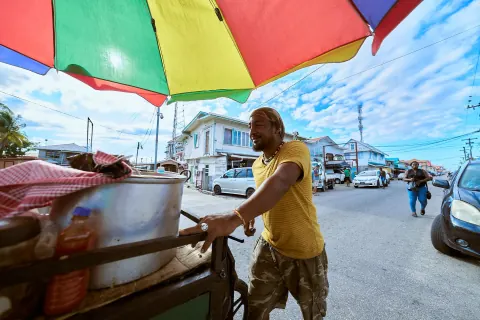 A street vendor beside a food cart under a multicoloured umbrella.